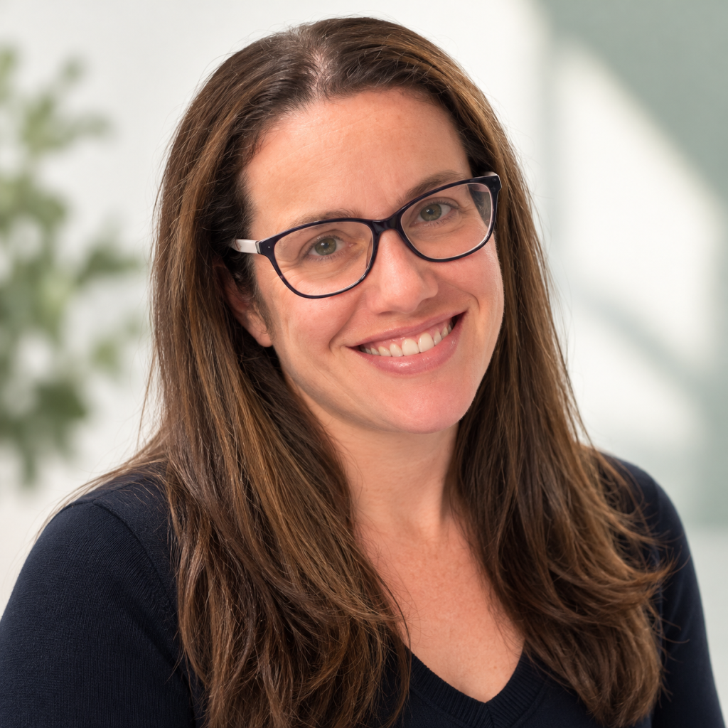 Danielle smiling, wearing dark-framed glasses and a navy sweater